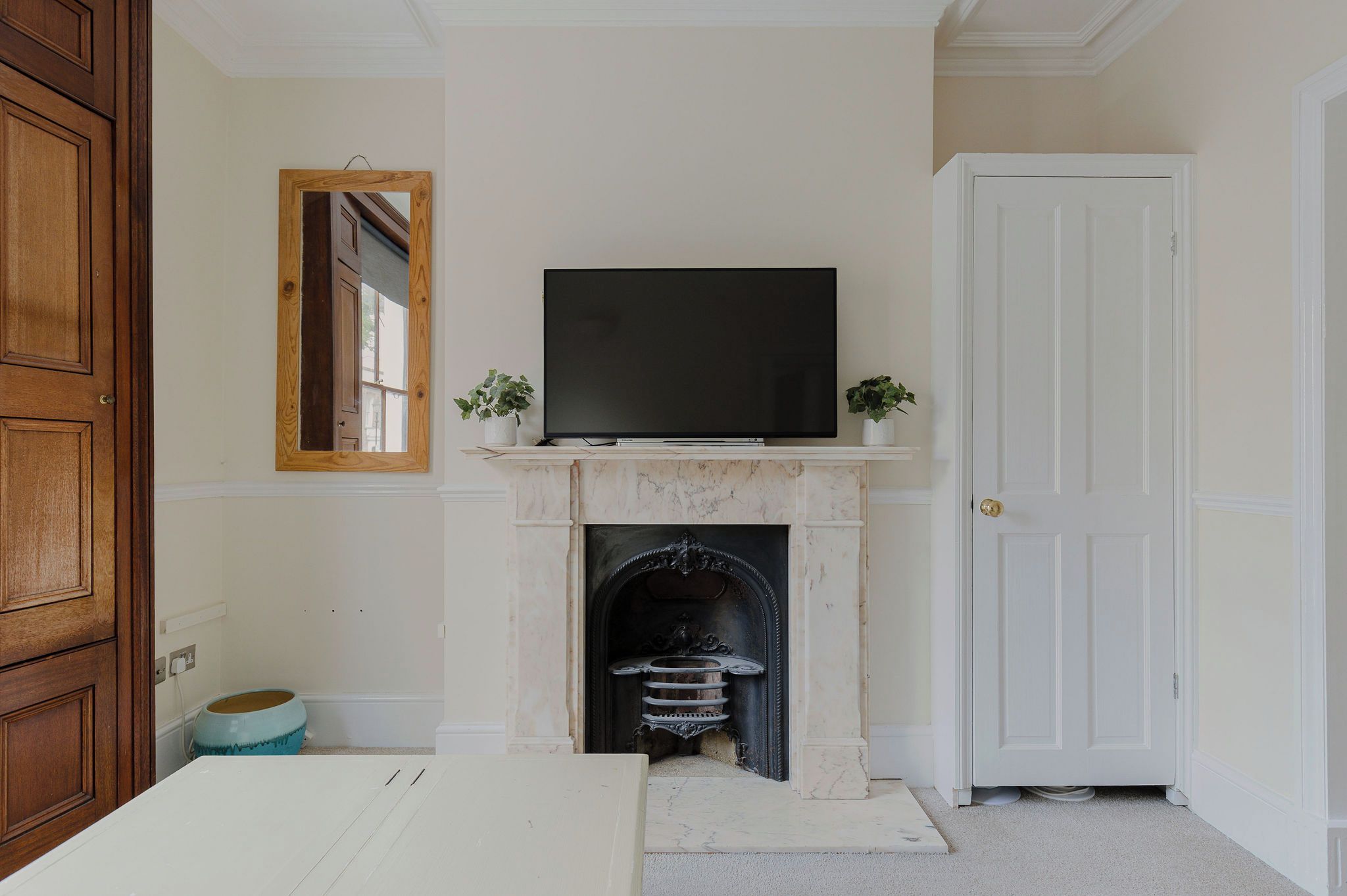 A room with a fireplace, a television mounted above it, a door, and a mirror on the wall.