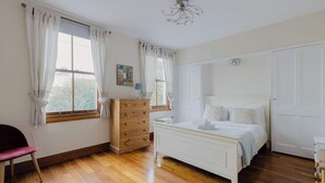 A bedroom with a wooden dresser, a bed, a chair, and a window with curtains. - Prime Location 2 Bed East London (London)
