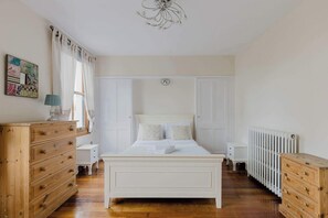 A bedroom with a white bed, wooden dresser, and radiator.