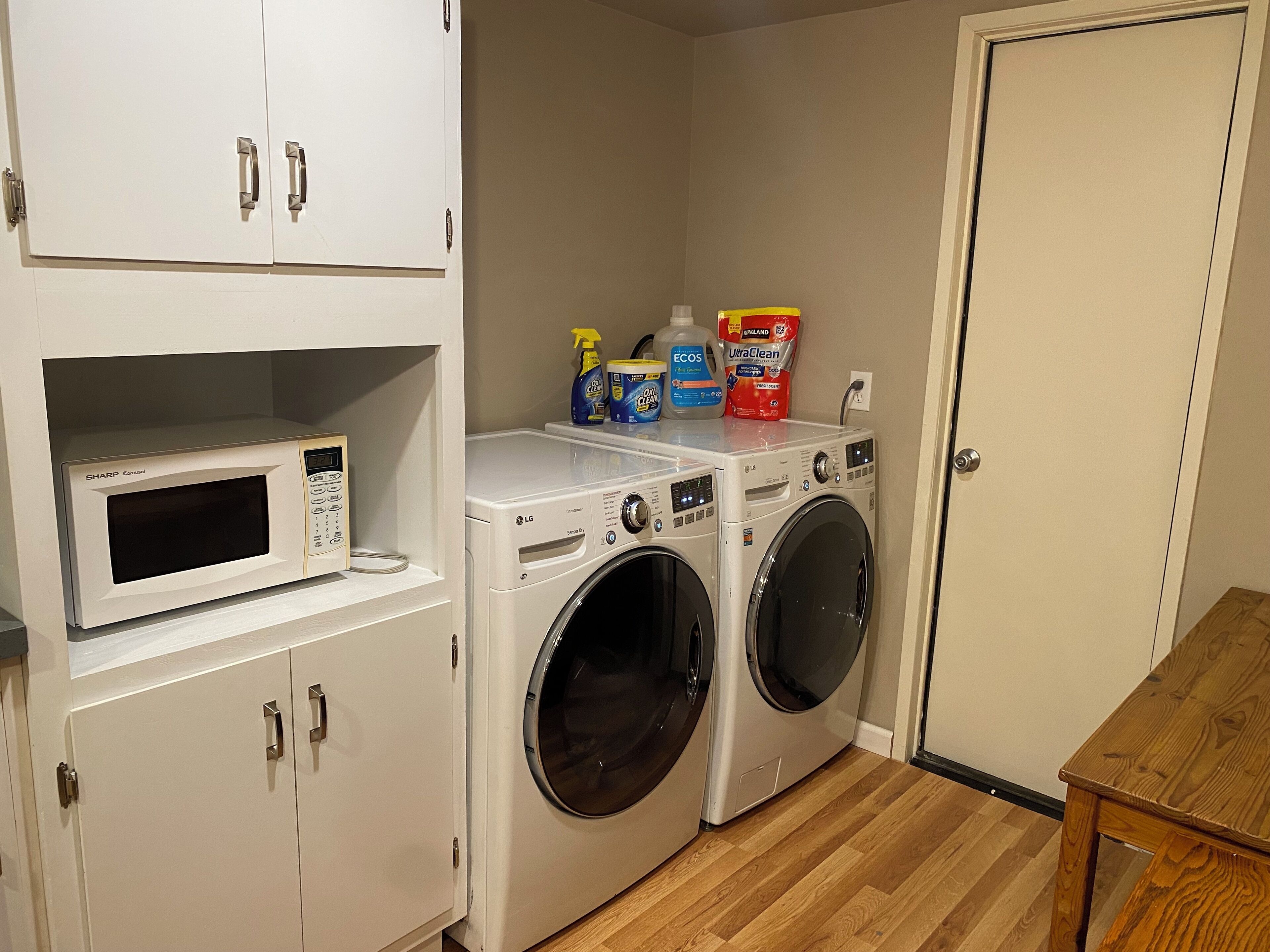 A laundry room with a microwave, two washing machines, and shelves with cleaning supplies.