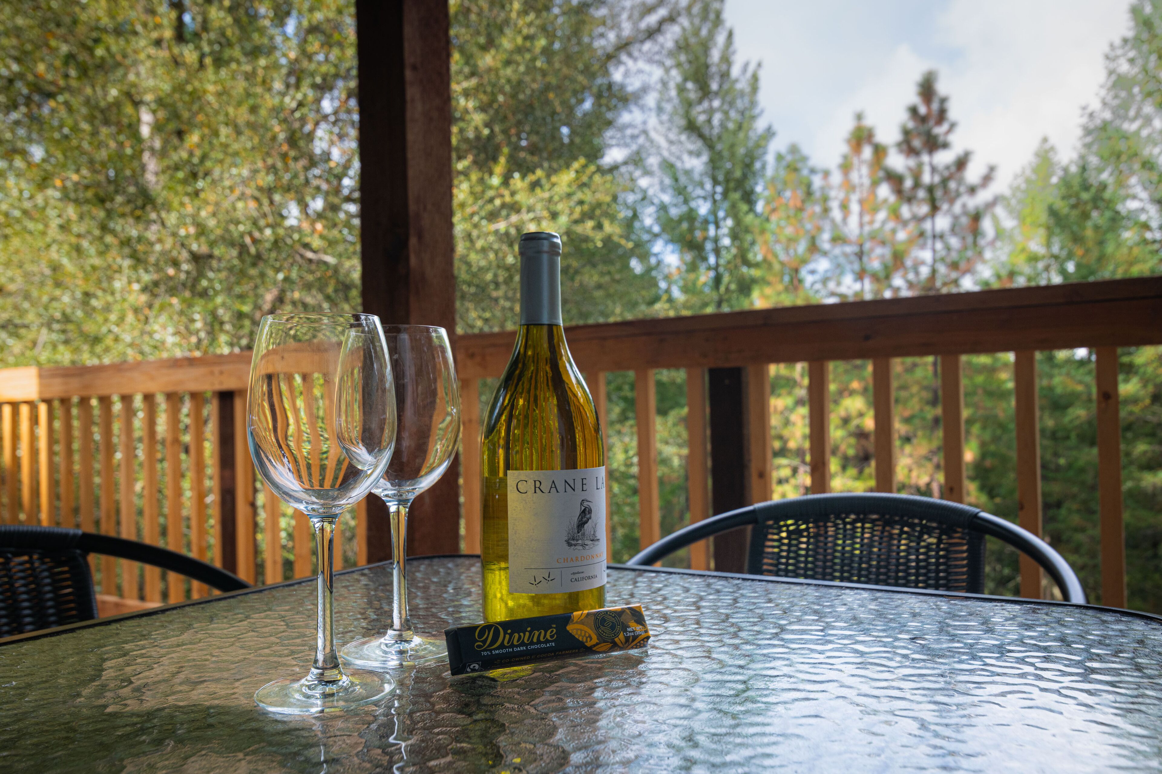 A glass table with a bottle of wine and a chocolate bar on a glass table outdoors.