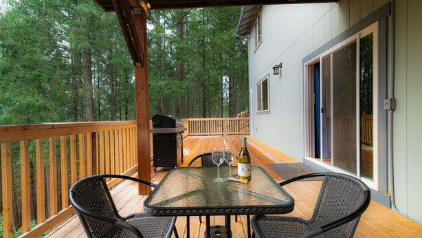 A covered outdoor deck with a table and chairs, a grill, and a bottle of wine. - Cobb Mountain Chalet King Size Suite (Cobb)