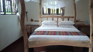 Een houten bed met hemelbed, witte beddengoed en een kleurrijke gestreepte deken.