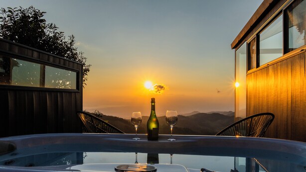 Un jacuzzi con una botella y vasos, con vista a una puesta de sol y montañas.