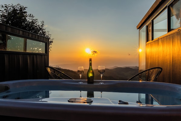 Un jacuzzi con una botella y vasos, con vista a una puesta de sol y montañas.