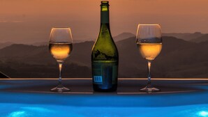 Una botella de vino y dos copas sobre una mesa, con vistas a montañas al atardecer.