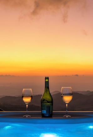 Une bouteille de vin et deux verres sur une table, avec vue sur les montagnes au coucher du soleil.