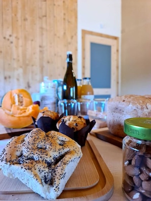 Una mesa de madera con diversos productos horneados, como un rollo de semillas de amapola, muffins y una barra de pan.