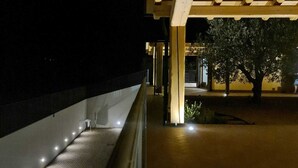 An outdoor area with a wooden pergola structure, a paved walkway, and a row of lights along the edge.