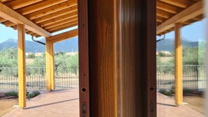 A covered outdoor area with wooden beams and a brick floor, featuring a view of a mountainous landscape.