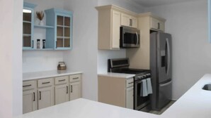 A modern kitchen with white and light blue cabinetry, a black microwave, a stainless steel refrigerator, and a white countertop. - Luxury Boho Bay House. Balcony with Sunset Views, Near Casinos & Beach (Pleasantville)
