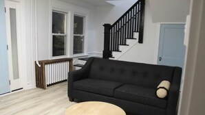 A living room with a black sofa, a round wooden coffee table, and a staircase with black railings. - Luxury Boho Bay House. Balcony with Sunset Views, Near Casinos & Beach (Pleasantville)