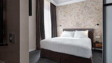 Una camera d'albergo moderna con un letto grande, tende scure, una parete con motivo geometrico e un comodino con una lampada.