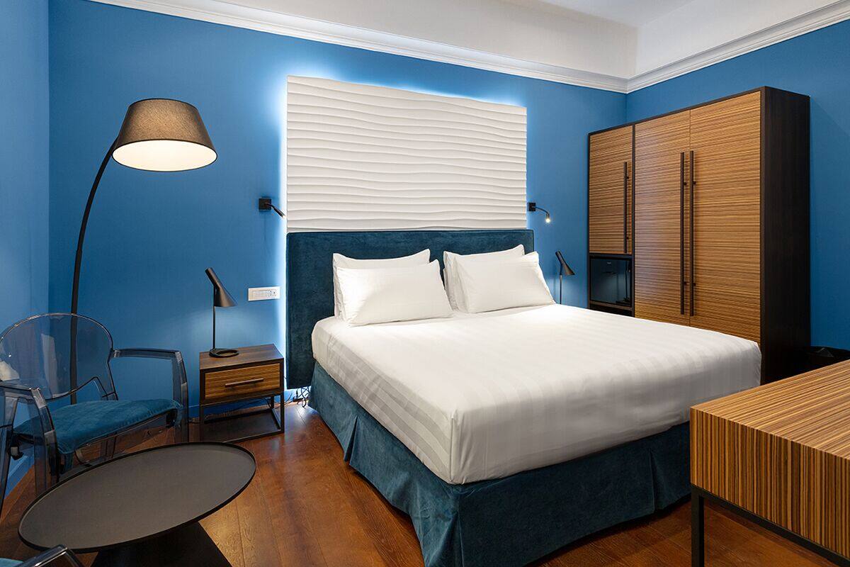 A bedroom with a bed, a desk, a chair, a wardrobe, and a lamp.