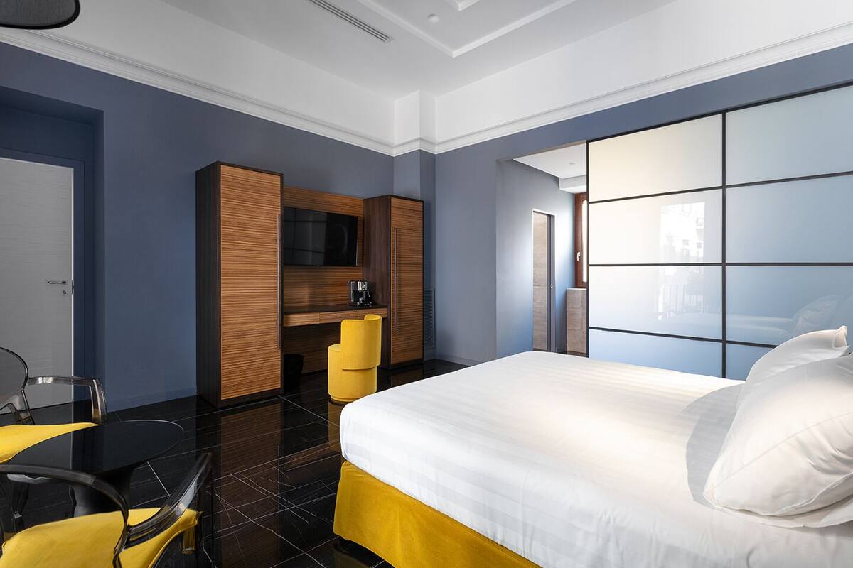 A modern hotel room with a large bed, a desk with a chair, a television, and a wardrobe.