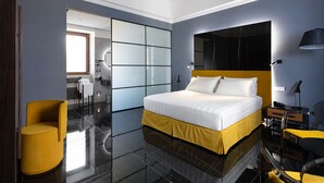 A modern hotel room with a large bed, a yellow armchair, a desk with a lamp, and a large mirror on the wall. - Poerio 25 Boutique Stay (Naples)