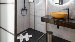 A modern bathroom with a glass-enclosed shower, a black sink with a yellow bowl, and a large mirror with a circular frame. - Poerio 25 Boutique Stay (Naples)