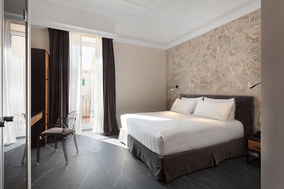 A hotel room with a large bed, a chair, a desk, and a view of the outside.