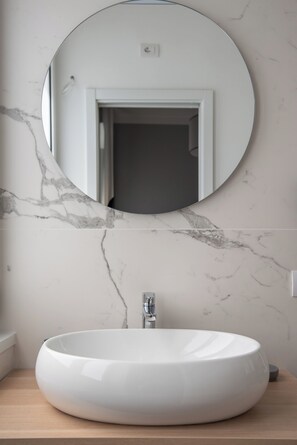 A bathroom with a round mirror above a white sink, a marble wall, and a wooden countertop. - Nolana 28 Rooms in Naples (Naples)