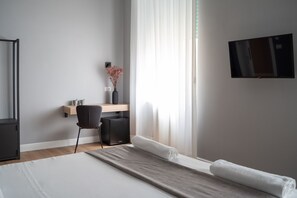 A modern hotel room with a bed, a desk, a chair, a TV, and a window with curtains. - Nolana 28 Rooms in Naples (Naples)