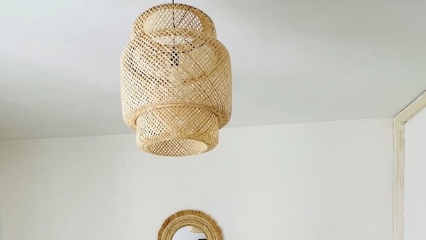 Ein neutral eingerichtetes Wohnzimmer mit einem beige gefärbten Sofa, einem runden Spiegel, einem gewebten Rattan-Tisch und einer hängenden Leuchte.