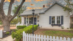 A single-story house with a porch, white picket fence, and a well-maintained lawn. - Awesome Haus With Gameroom, 4blks to Center of Town! (Fredericksburg)