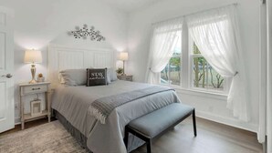 A bedroom with a bed, bedside tables, a bench, a window with curtains, and a decorative wall piece. - Awesome Haus With Gameroom, 4blks to Center of Town! (Fredericksburg)