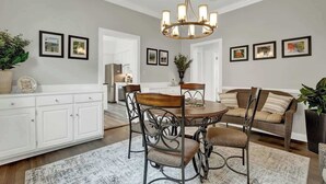 A dining area with a round table, chairs, and a chandelier. There are framed pictures on the walls and a sofa in the background. - Awesome Haus With Gameroom, 4blks to Center of Town! (Fredericksburg)