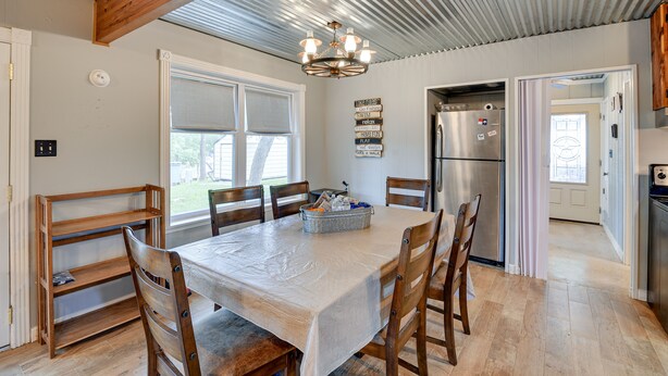 A modern kitchen with a dining area, featuring a large table, wooden chairs, a chandelier, and a refrigerator. - Lake Brownwood Home w/ Private Boat Dock! (Brownwood)