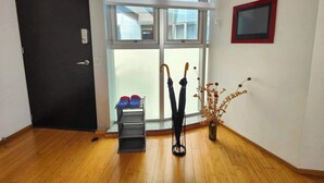 A room with a sliding glass door, a black door, a small shelf with blue shoes, two umbrellas, and a vase with dried flowers. - Lovely Condo Best City Location. (Mexico City)