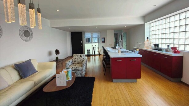 A modern kitchen with a central island, a dining area with a sofa and coffee table, and a living room with a patterned rug. - Lovely Condo Best City Location. (Mexico City)