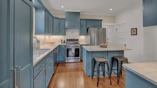 A modern kitchen with blue cabinets, a stainless steel refrigerator, and a wooden floor.