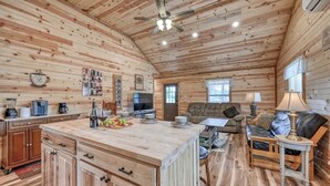 A rustic cabin interior with a wooden interior, a kitchen area with a central island, a sofa, and a dining table. - Cozy Cabin Firepit and Grill & 10 Mins to Main St (Fredericksburg)