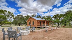 A wooden cabin with a porch, surrounded by outdoor seating and a fire pit. - Cozy Cabin Firepit and Grill & 10 Mins to Main St (Fredericksburg)