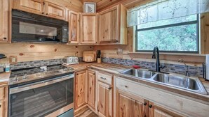 A wooden cabin kitchen with a large window, a built-in oven, and a sink. - Cozy Cabin Firepit and Grill & 10 Mins to Main St (Fredericksburg)