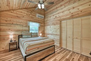 A wooden-paneled bedroom with a bed, bedside lamps, a ceiling fan, and a window. - Cozy Cabin Firepit and Grill & 10 Mins to Main St (Fredericksburg)
