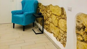 A room with a blue chair, a small table, a stone wall, and a white door. - Bardilio Luxury Rooms IUN P1813 (Cagliari)