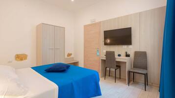 Habitación de hotel con cama, escritorio, dos sillas, televisor y armario.