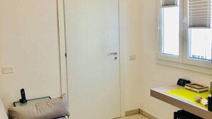 A small, well-lit room with a door, a sofa, a small table with a yellow mat, and a mini-fridge with beverages. - Bardilio Luxury Rooms IUN P1813 (Cagliari)
