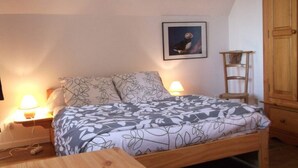 A bedroom with a bed, two bedside lamps, a wooden nightstand, a wooden chair, a wooden wardrobe, and a framed picture on the wall. - Appartement de 38 m2 au Sein D'une Petite Résidence Avec Jardin (Pont-l'Abbé)