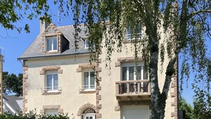 A two-story house with a stone facade, a front door, and a small balcony with outdoor furniture. - Appartement de 38 m2 au Sein D'une Petite Résidence Avec Jardin (Pont-l'Abbé)
