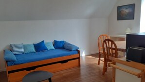 A room with a wooden bed, a small table, a chair, and a desk with a lamp. - Appartement de 38 m2 au Sein D'une Petite Résidence Avec Jardin (Pont-l'Abbé)