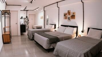 Ein Hotelzimmer mit drei Betten, einer kleinen Küchenzeile, einem Badezimmer und einem Kleiderständer.
