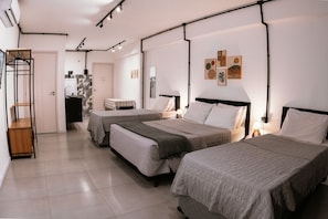 Una habitación de hotel con tres camas, una kitchenette pequeña, un baño y un perchero.