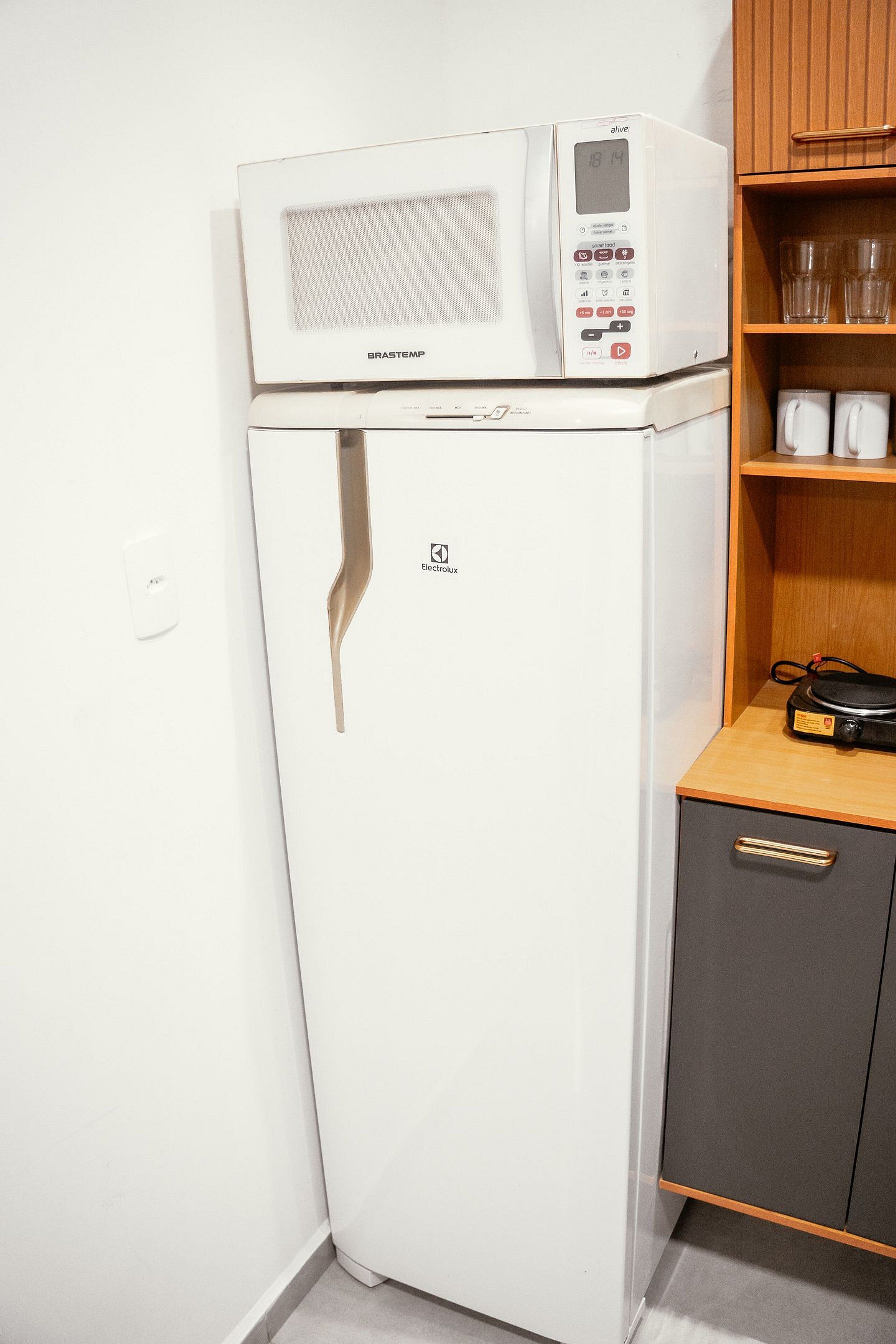 Una kitchenette compacta con un refrigerador blanco, un microondas encima y un pequeño armario con algunos artículos.