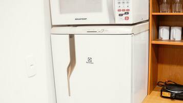 Una kitchenette compacta con un refrigerador blanco, un microondas encima y un pequeño armario con algunos artículos.