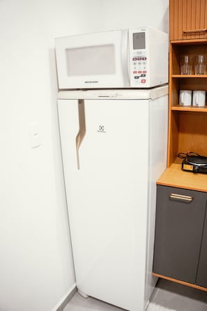 Una kitchenette compacta con un refrigerador blanco, un microondas encima y un pequeño armario con algunos artículos.
