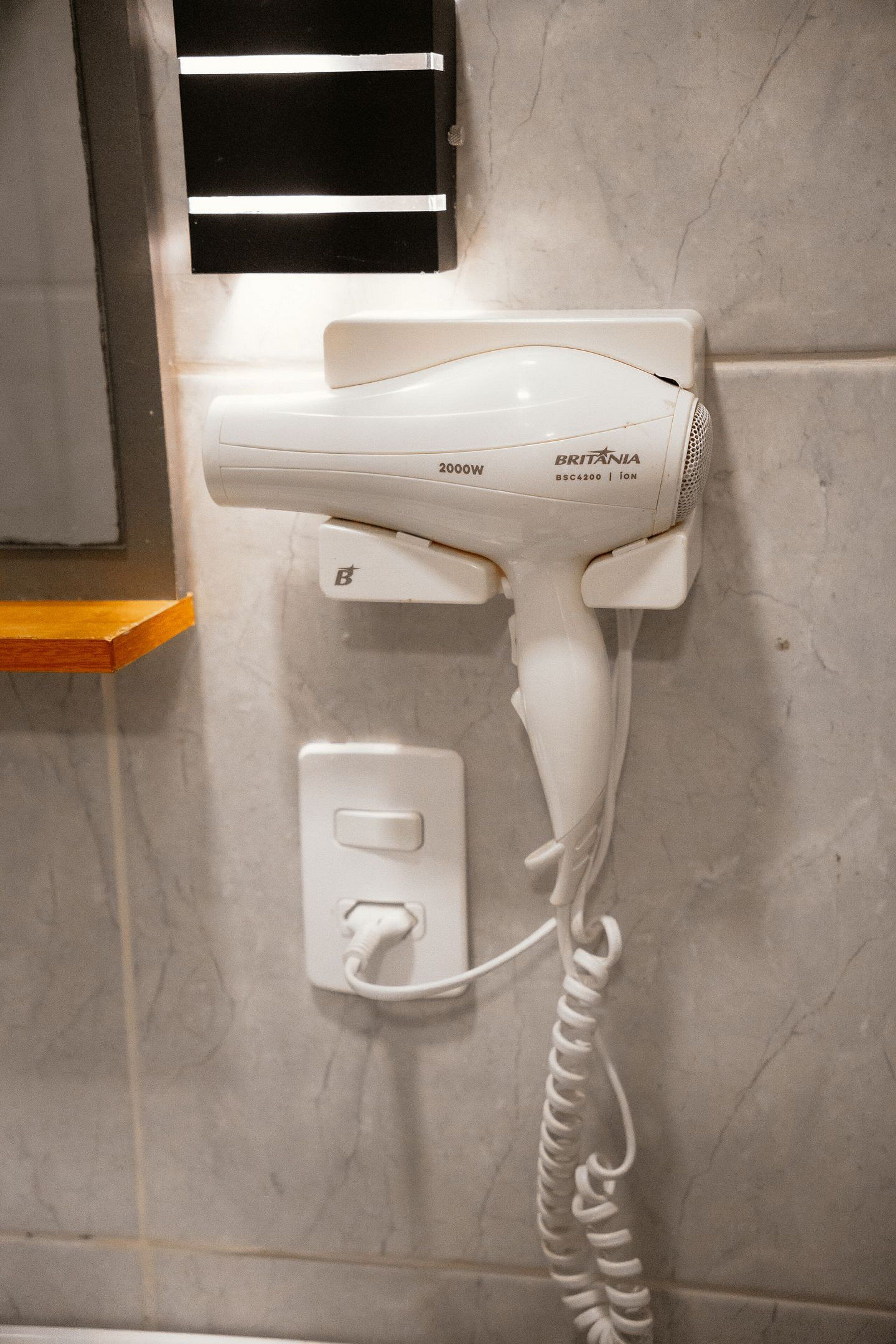 Un secador de pelo montado en la pared con cable, un enchufe e interruptor.
