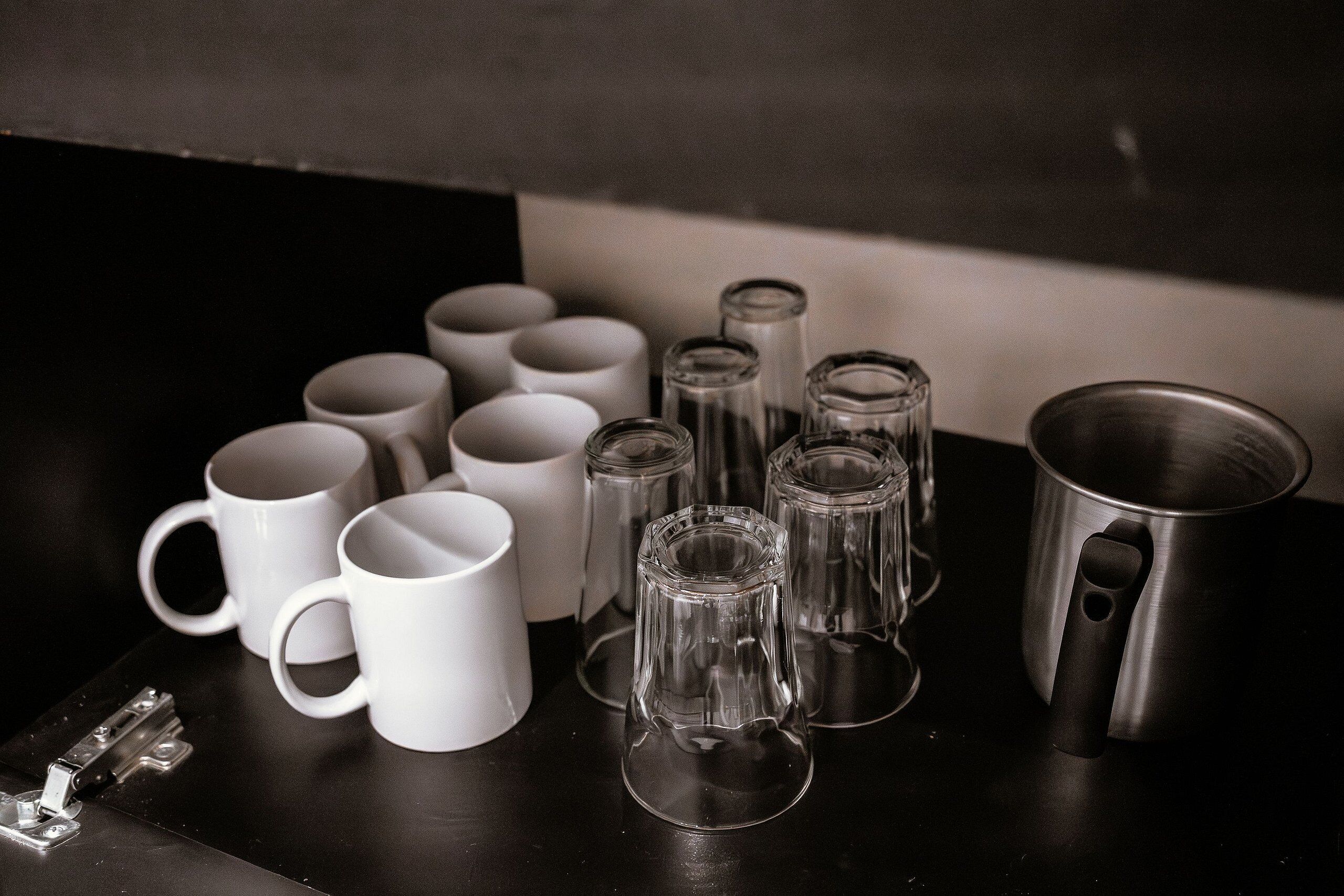 Une collection de tasses blanches et de verres transparents posée sur une surface sombre.