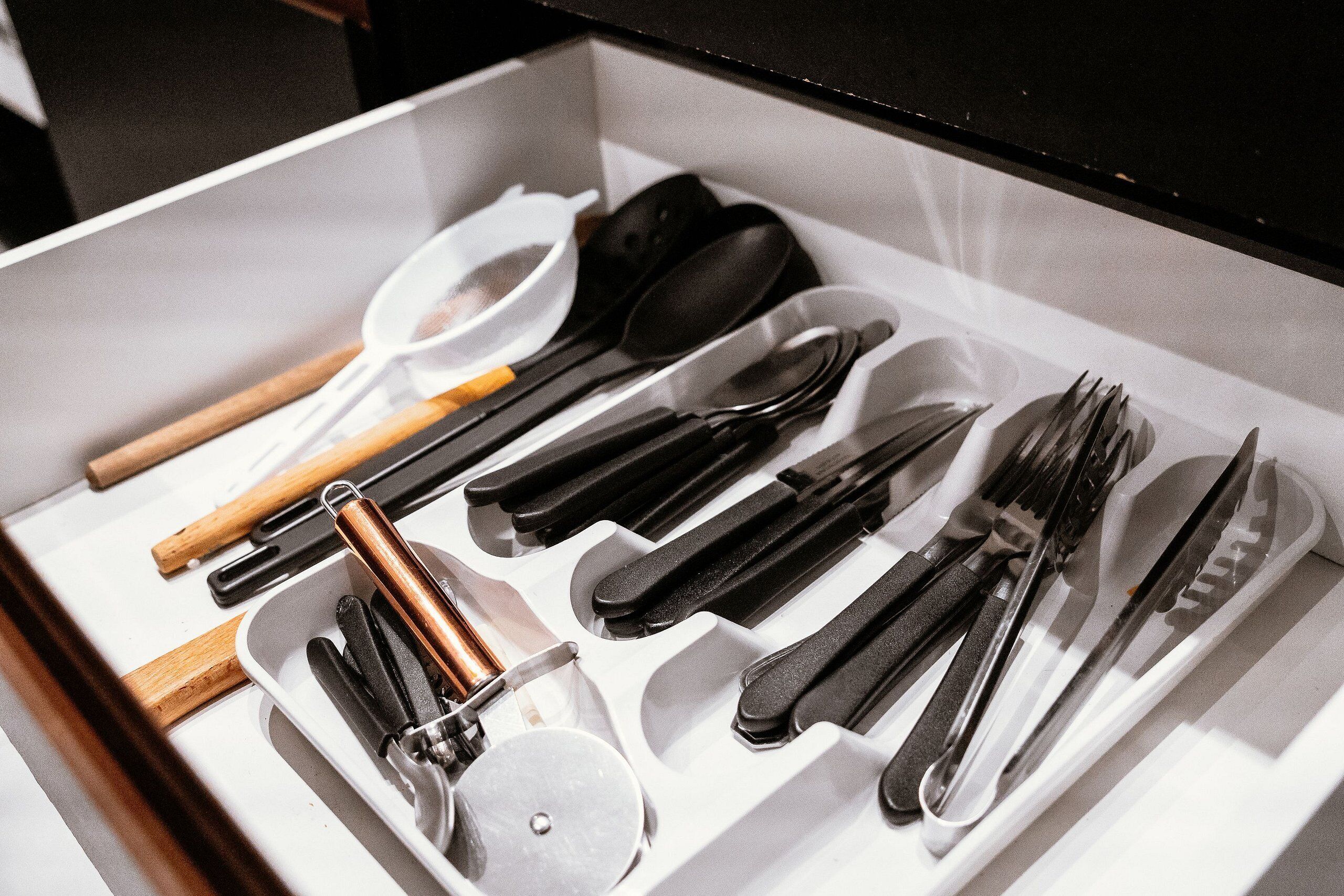 Un cajón con diversos utensilios de cocina ordenados, incluyendo cucharas, tenedores, cuchillos y un par de pinzas.